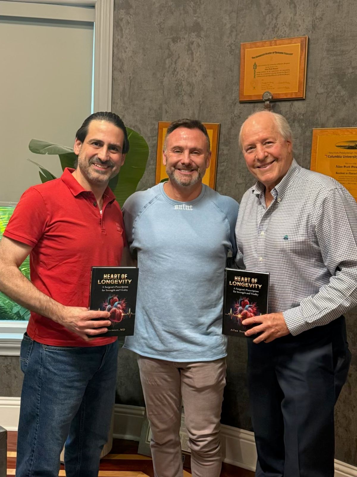 Dr. Allan Stewart with two men holding copies of his book, Heart of Longevity
