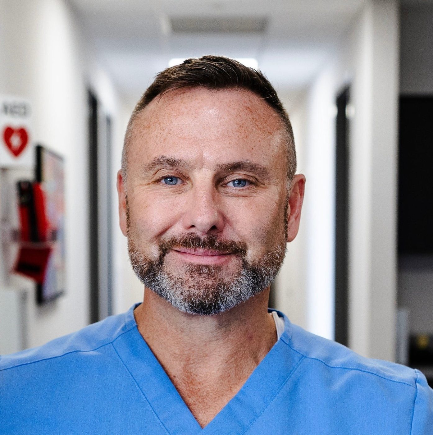 Dr. Allan Stewart in blue scrubs, smiling, in a hallway
